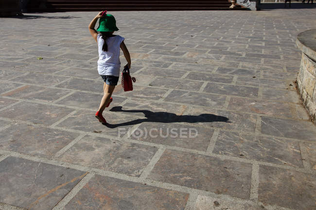 Вид сзади на девушку в шляпе, бегущую по улице — стоковое фото