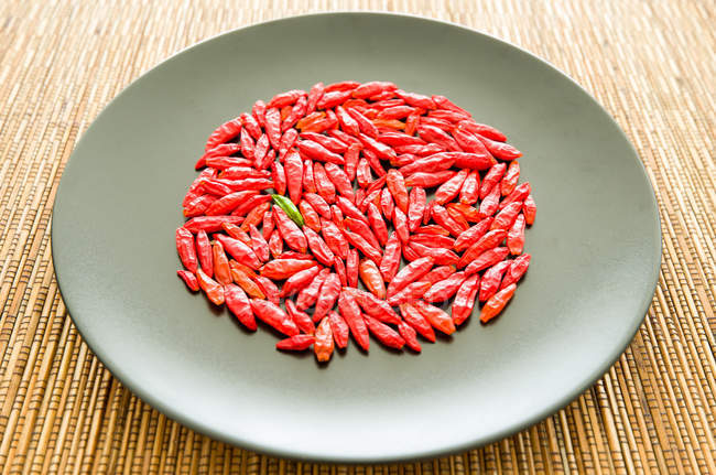 Peperoncino verde circondato da peperoncini rossi su un piatto — Foto stock