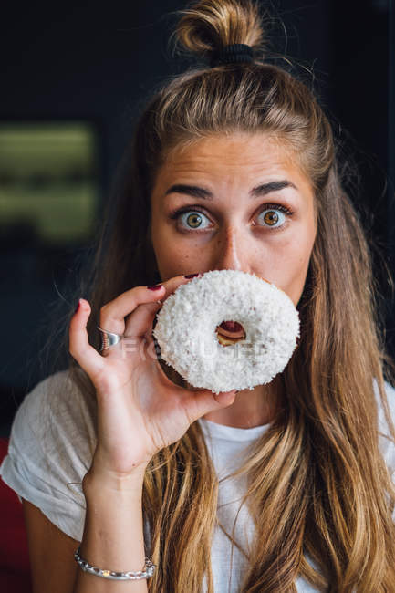 Красива молода жінка тримає пончик перед обличчям — стокове фото
