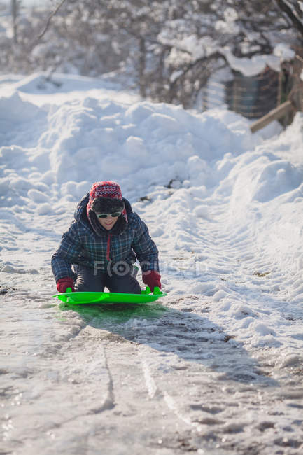 Heureux garçon agenouillé sur luge dans la neige — Photo de stock