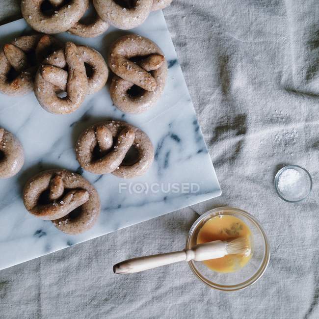 Homemade pretzels on white marble and bowl with egg yolk — Stock Photo