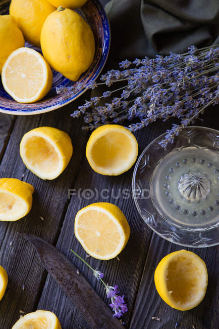 Limones a la mitad y enteros con flores de lavanda sobre mesa de madera - foto de stock