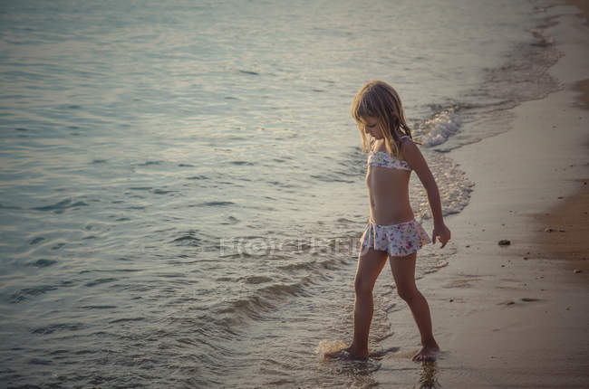 Fille debout et jouer avec l'eau sur la plage de sable — Photo de stock