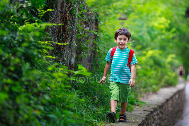 Garçon avec sac à dos marchant sur le mur de pierre dans le parc — Photo de stock