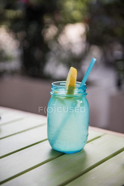 Glass of blue lemon water with drinking straw on table against blurred background — Stock Photo