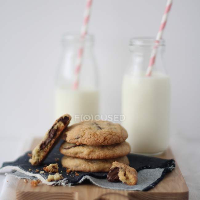 Pila di biscotti al cioccolato con bottiglie di latte su sfondo di legno — Foto stock