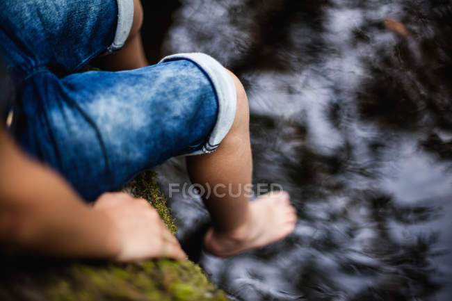 Primer plano de Niño sentado al borde de un río - foto de stock