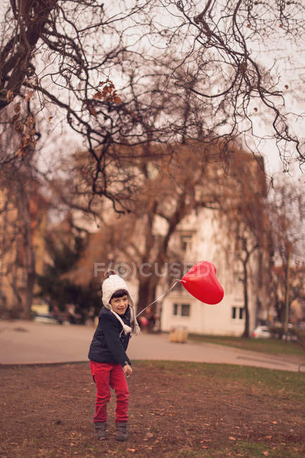 Boy playing with heart-shaped red balloon outdoors — Stock Photo