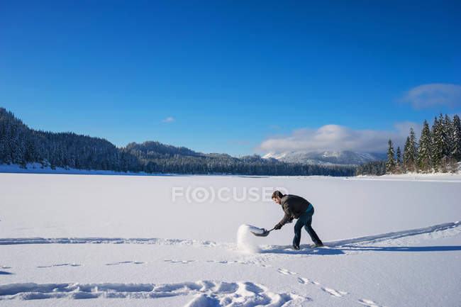Людину, лопатою сніг в полі з синього неба на тлі — стокове фото