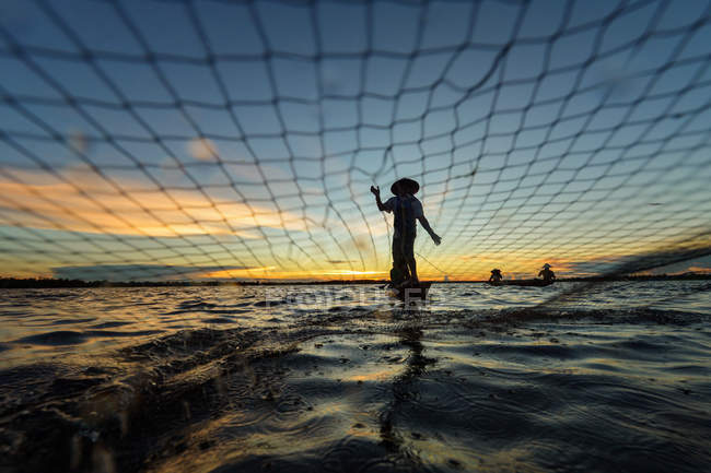 Silhouette eines Fischers, der im Boot steht und bei Sonnenuntergang das Netz zieht, nongkhai, Thailand — Stockfoto