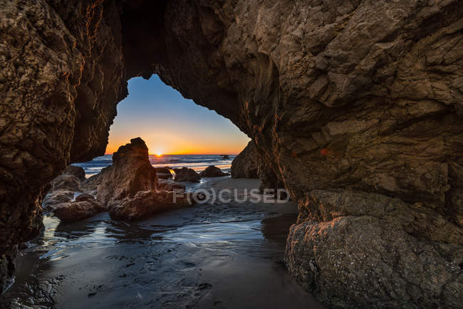 Vista panorámica de la puesta de sol a través de rocas, playa de El Matador, Malibú, California, América, EE.UU. - foto de stock