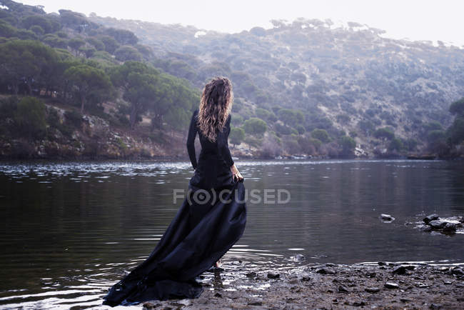 Donna vestita di nero che cammina in acqua nella natura — Foto stock