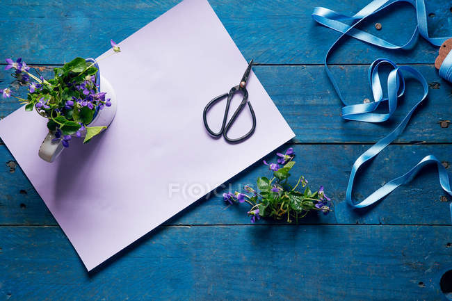 Spring flowers, ribbon, scissors and paper on blue wooden table — Stock Photo
