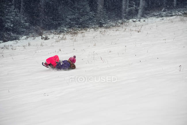 Chica divirtiéndose en un trineo en la pendiente en invierno - foto de stock