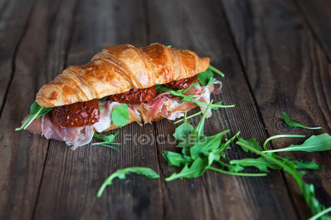 Бутерброд з круасанами з прошутто, сушеними помідорами та руколою — стокове фото