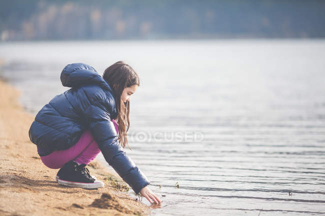 Fille accroupi au lac et toucher l'eau — Photo de stock
