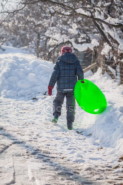 Хлопчик ходить у снігу, несучи санки — стокове фото