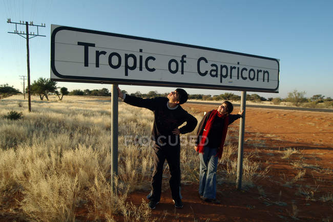 Підліток хлопчик і дівчинка стоїть під тропіка Козерога знак, Намібія — стокове фото