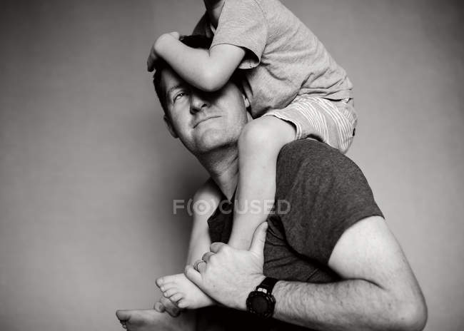 Black and white photo of Cute little boy sitting on father shoulders — Stock Photo