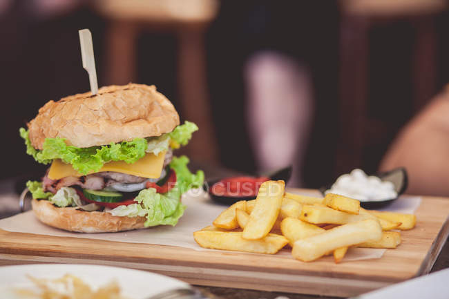 Hamburger and fries over wooden board against blurred background — Stock Photo