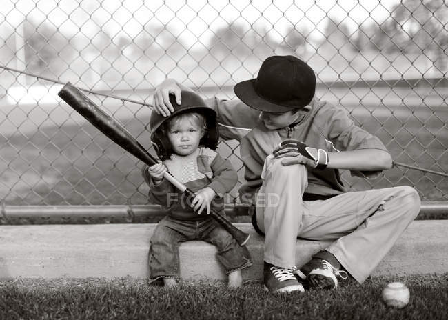 Монохромне зображення двох кавказьких хлопчиків з бейсбольною битою, що сидить на дворі — стокове фото