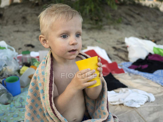 Garçon debout sur la plage et tenant tasse en plastique — Photo de stock