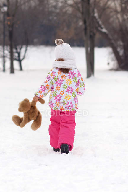 Вид спереду дівчини, що йде з плюшевим ведмедем взимку — стокове фото