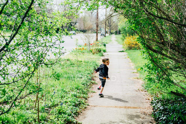 Хлопчик біжить уздовж тротуару, дивлячись через плече — стокове фото