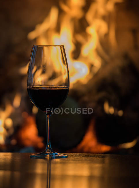 Glass of red wine on a table in front of a fireplace — Stock Photo