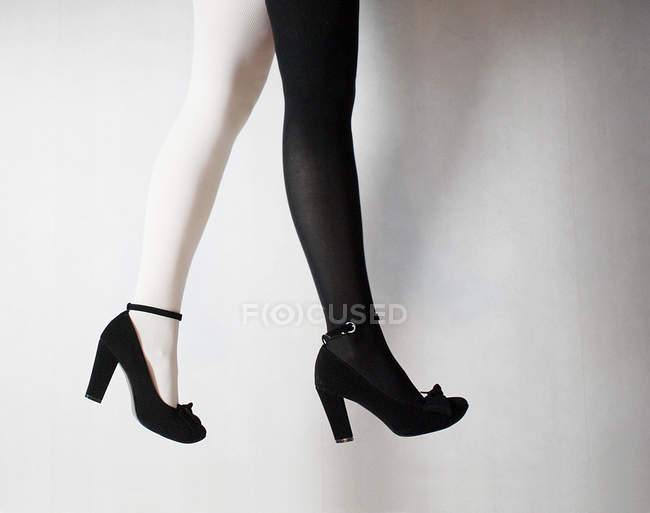 Обрезанное изображение женских ног с двумя цветными колготками, на черных каблуках — стоковое фото