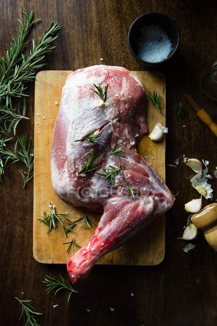 Still life of lamb leg and herbs over chopping board — Stock Photo