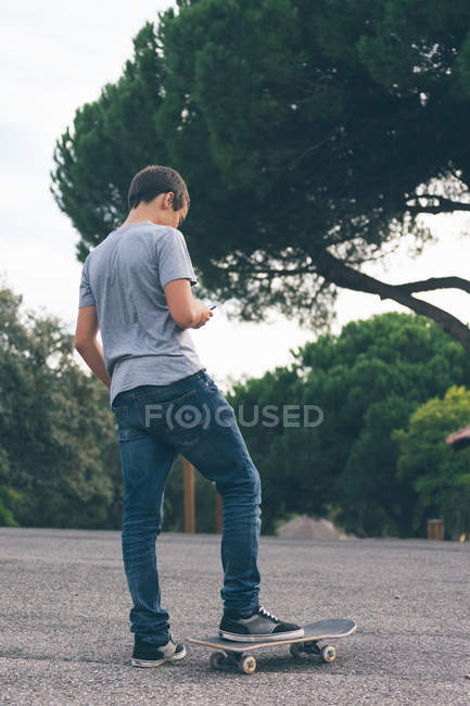 Boy texting on mobile phone while skateboarding in park — Stock Photo
