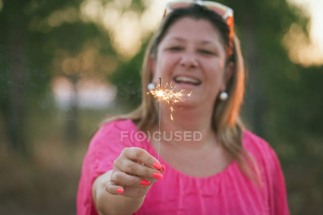 Retrato de una mujer de mediana edad feliz sosteniendo chispa y riendo - foto de stock