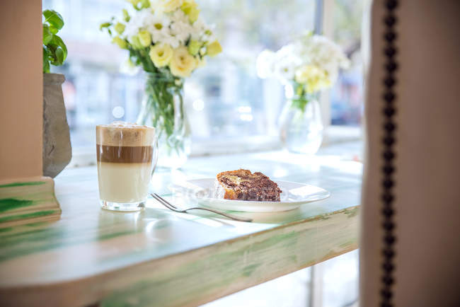 Café cappuccino com fatia de bolo no peitoril da janela — Fotografia de Stock