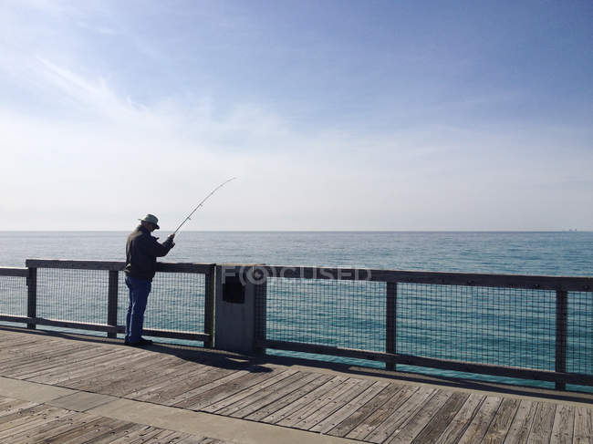Uomo anziano pesca sul molo di legno in mare — Foto stock