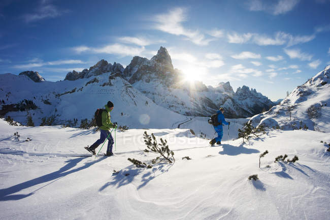 Вид збоку двох сміливих мандрівників, що ходять у засніжених горах з лижами — стокове фото