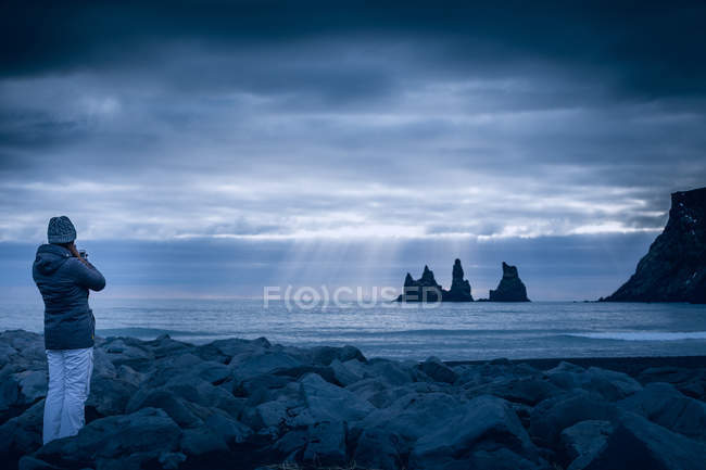 Mulher de pé no mar sobre nuvens tempestuosas e olhando para a vista, Islândia — Fotografia de Stock