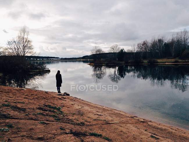 Silhouette di una donna in piedi sulla riva del lago e guardando la vista — Foto stock