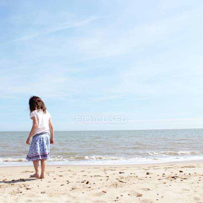 Little girl standing on sandy beach — Stock Photo