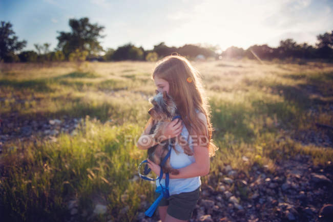 Девушка с длинными волосами, несущая собаку в природе — стоковое фото