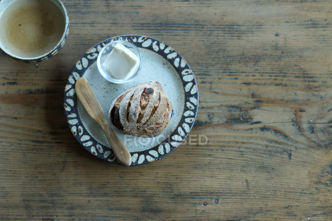 Bread roll and butter on plate on wooden surface — Stock Photo