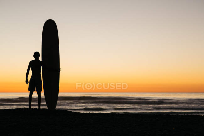 Surfista y su tabla disfrutando de un resplandor post surf noche - foto de stock