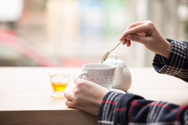 Cropped image of Woman putting honey in cup of tea — Stock Photo