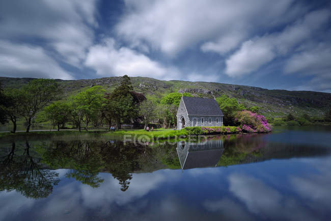 Irlanda, Condado de Cork, Gouganne barra, vista panorámica de la capilla junto al lago reflejándose en el agua - foto de stock