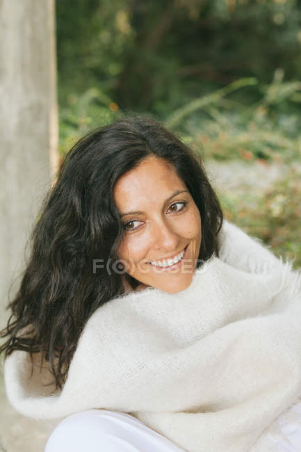 Mujer sonriente envuelta en manta sentada en la terraza - foto de stock