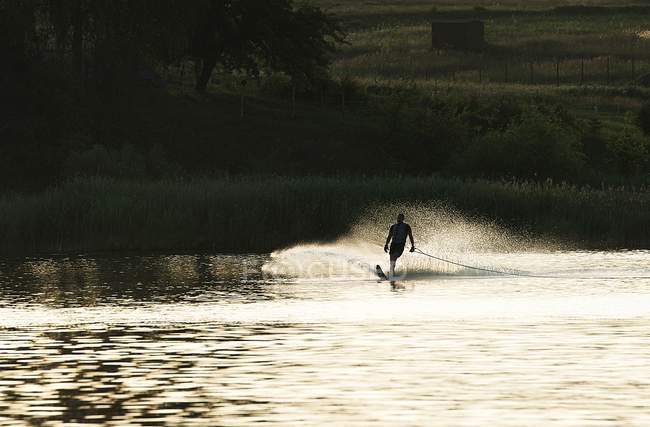 Силуэт человека, пробуждающегося на озере на закате — стоковое фото