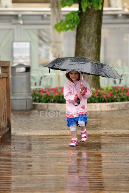Girl wearing raincoat holding umbrella on wooden path — Stock Photo