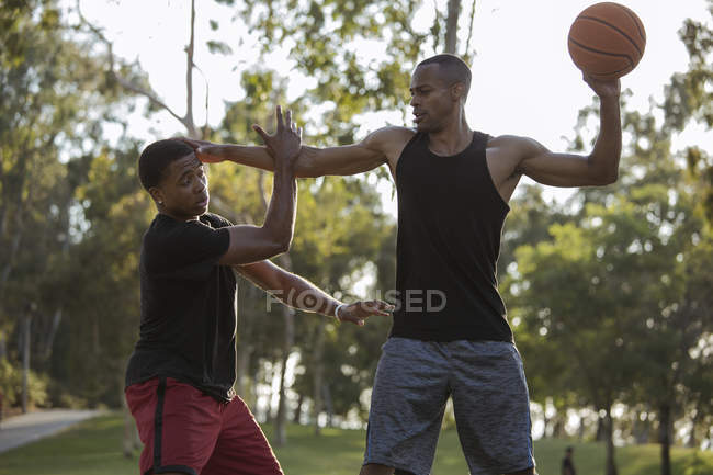Баскетболіст тримає суперника в парку на заході сонця — стокове фото
