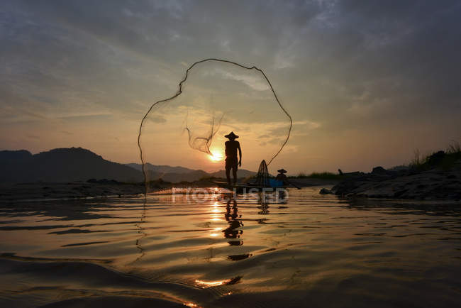 Silhouette of Man gettando cesto di pesca nel fiume Mekong, Thailandia — Foto stock