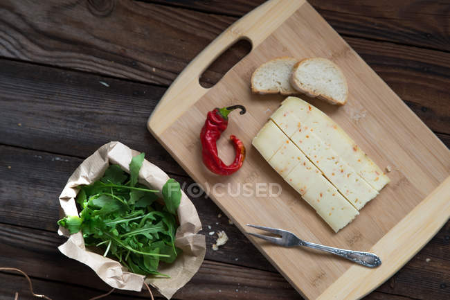 Vista elevada de queijo, pimenta, rúcula e pão sobre mesa de madeira — Fotografia de Stock